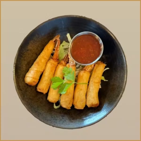 Golden-fried shrimp spring rolls with a side of red dipping sauce and a cilantro garnish.