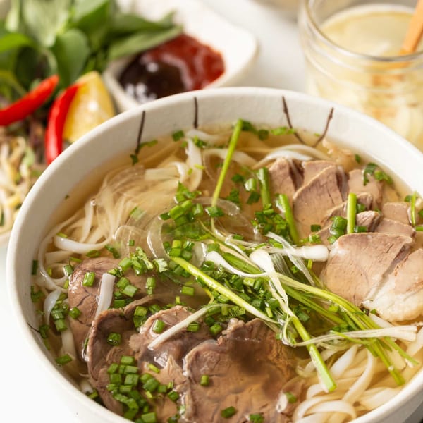 A close-up of a bowl of Pho La La's Vietnamese pho with beef, noodles, and green onions.