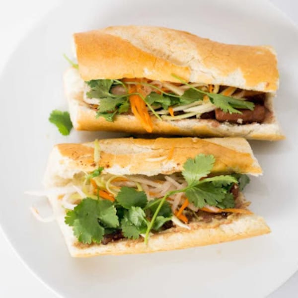 Two Vietnamese banh mi sandwiches with meat, pickled vegetables, and cilantro on a white plate.